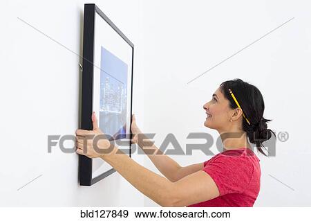 Stock Photo - Mixed race woman hanging painting. Fotosearch