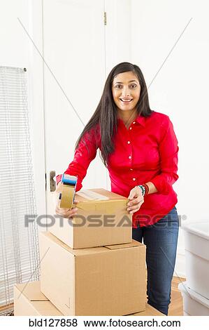 Stock Photo - Mixed race woman packing cardboard boxes. Fotosearch