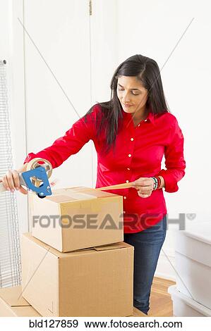 Stock Photo - Mixed race woman packing cardboard boxes. Fotosearch