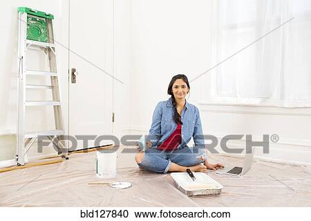 Stock Image - Mixed race woman relaxing while painting room. Fotosearch