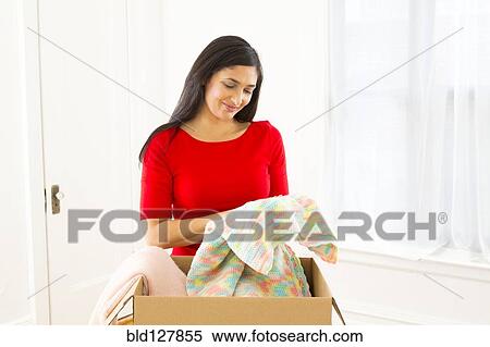 Stock Photography - Mixed race woman unpacking cardboard box. Fotosearch