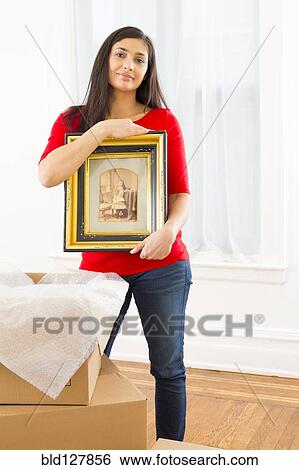 Stock Photograph - Mixed race woman unpacking cardboard boxes. Fotosearch