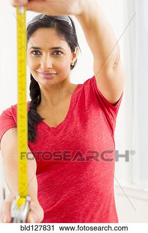 Stock Image - Mixed race woman using measuring tape. Fotosearch