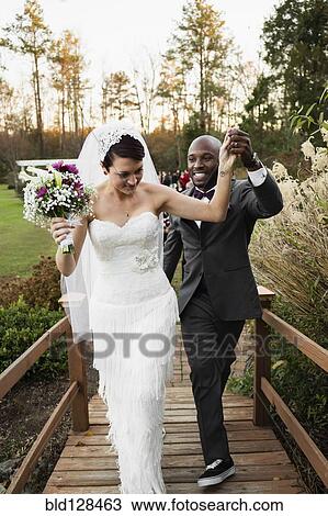 Stock Image - Newlywed couple walking on wooden footbridge. Fotosearch