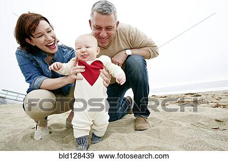 Parents helping baby walk on beach View Large Photo Image Stock Photo - Parents helping baby walk on beach. Fotosearch