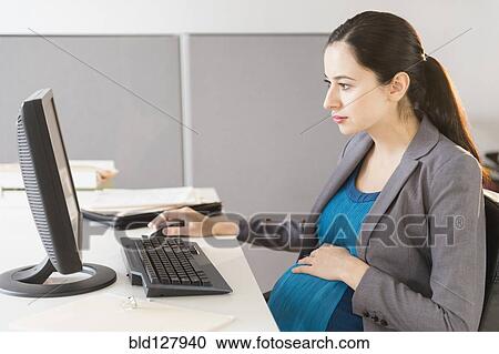 Stock Image - Pregnant Caucasian businesswoman working in office. Fotosearch