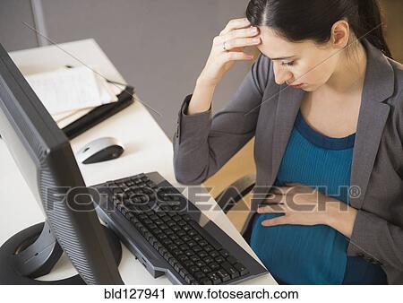 Stock Image - Pregnant Caucasian businesswoman working in office. Fotosearch