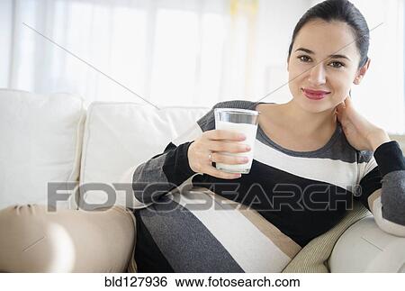 Stock Photograph - Pregnant Caucasian woman drinking milk on sofa. Fotosearch