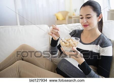 Picture - Pregnant Caucasian woman eating on sofa. Fotosearch