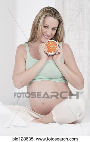 Stock Photography - Pregnant Caucasian woman holding alarm clock. Fotosearch
