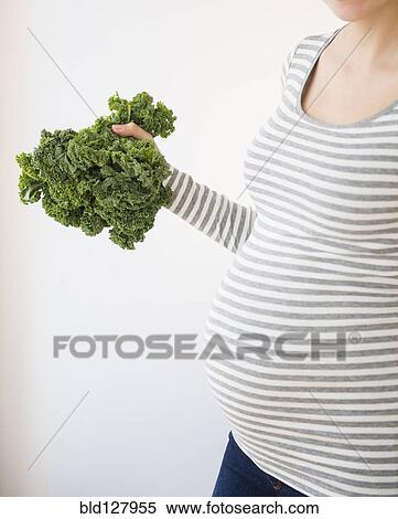 Stock Photography - Pregnant Caucasian woman holding head of kale. Fotosearch