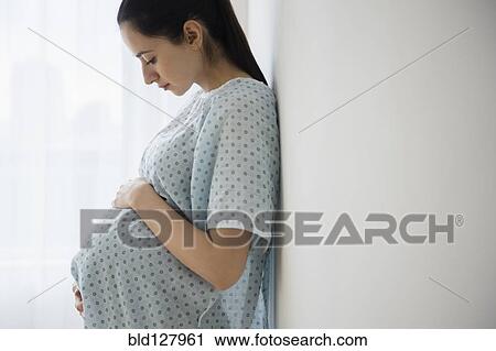 Stock Image - Pregnant Caucasian woman holding her belly in hospital. Fotosearch