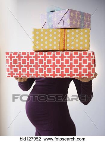 Stock Image - Pregnant Caucasian woman holding wrapped gifts. Fotosearch