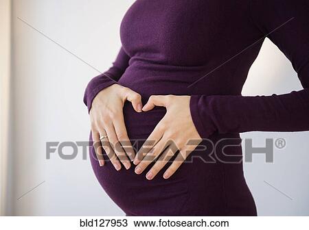 Stock Image - Pregnant Caucasian woman making heart shape on belly. Fotosearch