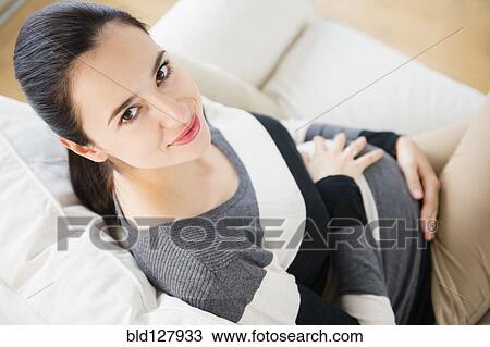 Stock Image - Pregnant Caucasian woman on sofa. Fotosearch