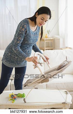 Stock Image - Pregnant Caucasian woman setting up baby chair. Fotosearch