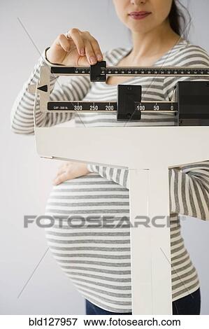 Stock Photo - Pregnant Caucasian woman weighing herself. Fotosearch