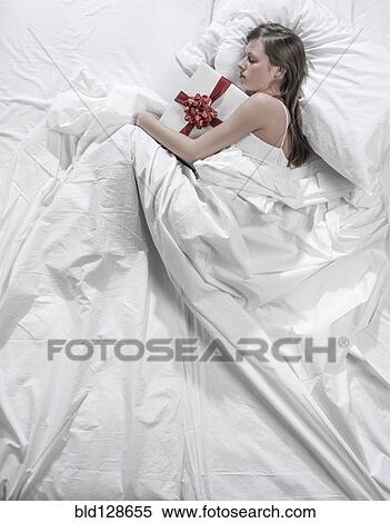 Stock Photography - Sleeping Hispanic woman hugging wrapped gift. Fotosearch