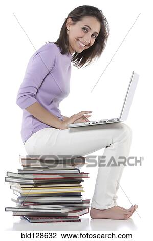 Stock Image - Woman using laptop on stack of books. Fotosearch