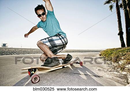 Stock Photography - Caucasian man riding longboard on beach. Fotosearch