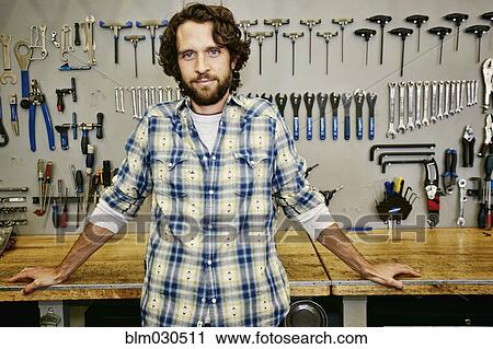 Stock Image - Caucasian man smiling in bicycle repair shop. Fotosearch