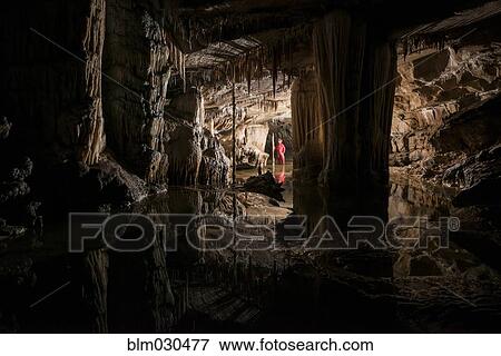 Stock Photo - Hiker exploring stalactites in cave. Fotosearch