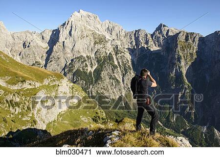 Stock Image - Hiker photographing craggy mountains, Mangart, Bovsko, Slovenia. Fotosearch