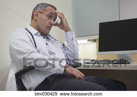 Stock Photo - Mixed race doctor rubbing his forehead in hospital. Fotosearch
