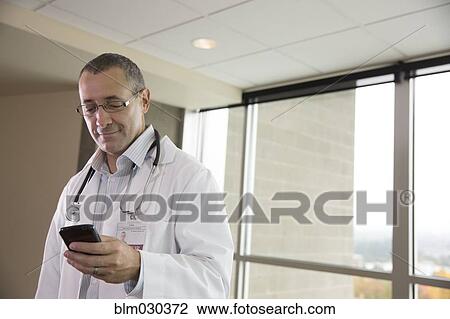 Stock Image - Mixed race doctor using cell phone in hospital. Fotosearch