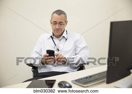 Stock Image - Mixed race doctor using cell phone in office. Fotosearch