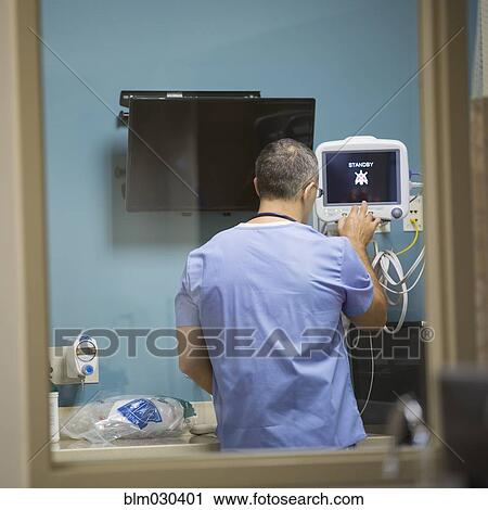 Stock Image - Mixed race doctor using machinery in hospital. Fotosearch