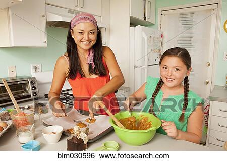 Stock Photograph - Mixed race mother and daughter baking in kitchen. Fotosearch