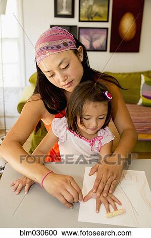 Stock Image - Mixed race mother and daughter coloring in kitchen. Fotosearch