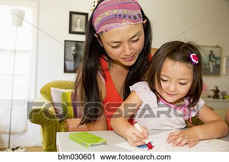 Stock Image - Mixed race mother and daughter coloring in kitchen. Fotosearch