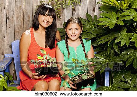 Stock Image - Mixed race mother and daughter holding potted plants. Fotosearch