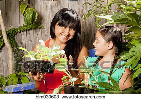 Stock Image - Mixed race mother and daughter holding potted plants. Fotosearch