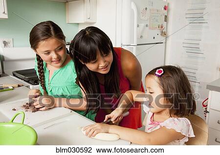 Stock Image - Mixed race mother and daughters baking in kitchen. Fotosearch