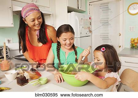 Stock Photography - Mixed race mother and daughters baking in kitchen. Fotosearch