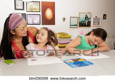 Stock Photo - Mixed race mother and daughters coloring in kitchen. Fotosearch