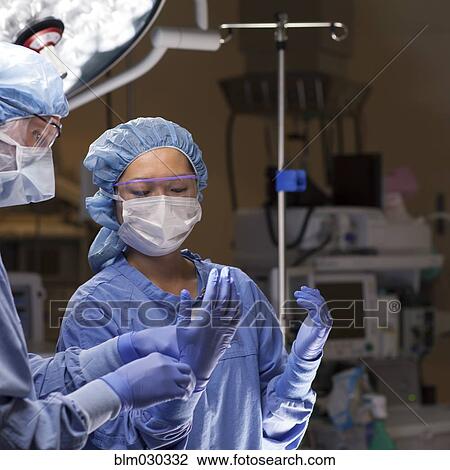 Stock Image - Nurse adjusting surgeon's gloves in operating room. Fotosearch