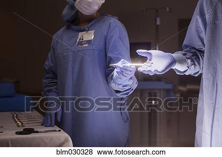 Stock Photo - Nurse handing implements to surgeon in operating room. Fotosearch
