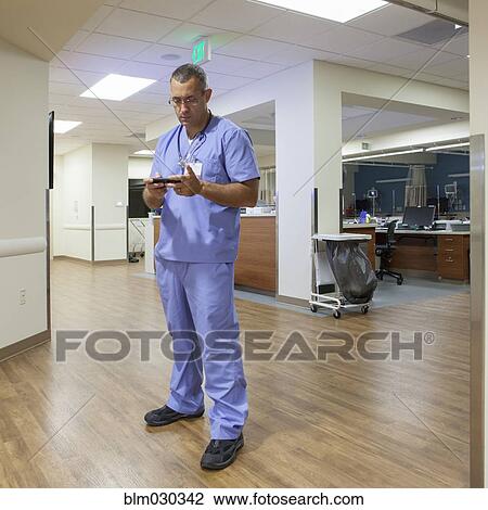 Stock Image - Nurse using cell phone in hospital corridor. Fotosearch