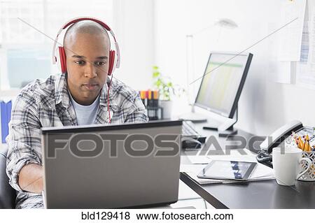 Stock Photo - Black businessman listening to headphones in office. Fotosearch