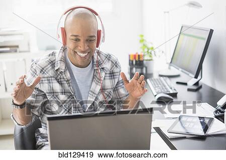 Black businessman listening to headphones in office View Large Photo Image Stock Photo - Black businessman listening to headphones in office. Fotosearch