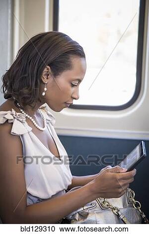 Stock Image - Black businesswoman using digital tablet on train. Fotosearch