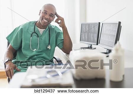 Black doctor smiling at computer in office View Large Photo Image Stock Photo - Black doctor smiling at computer in office. Fotosearch