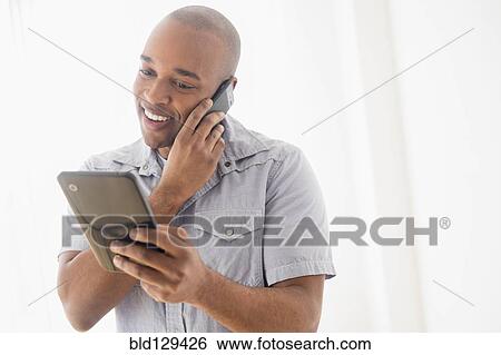 Stock Photograph - Black man using digital tablet and cell phone. Fotosearch