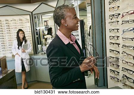Stock Image - Black woman trying on glasses at optometrist. Fotosearch