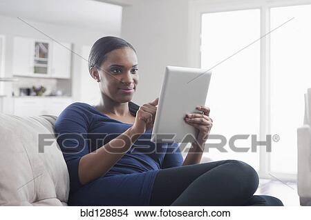 Picture - Black woman using digital tablet on sofa. Fotosearch