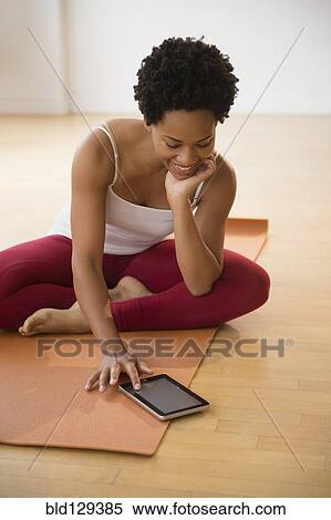 Stock Photography - Black woman using digital tablet on yoga mat. Fotosearch